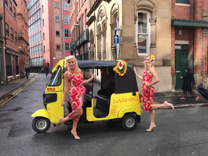 Mahiki branded yellow tuk tuk with two hosts at a launch